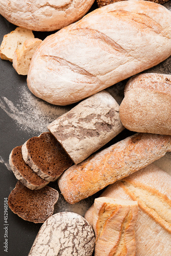 Lots of different fresh breads on a dark background. Fragrant airy baked goods. Sliced ​​piece of bread.
