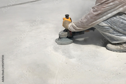 Close up of worker's hands using angle grinder. Removing of bleeding cement. Construction worker grinds concrete making clouds of dust