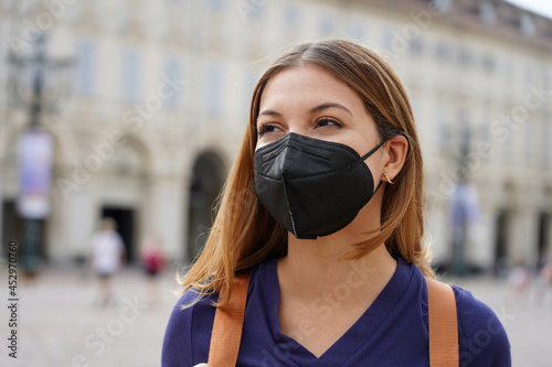 Portrait of student girl wearing a protective KN95 FFP2 black mask walking in city street photo