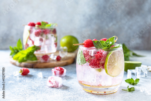Hard seltzer cocktail with raspberries and lime on a gray stone table top. Copy space.