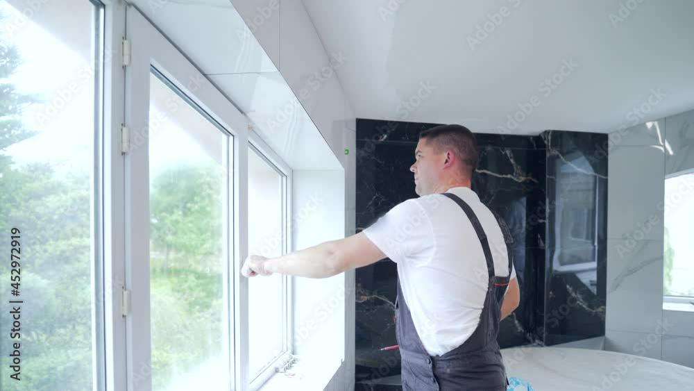 worker installs and adjusts a new plastic window in house. repair regulates Installation and adjustment Workman in overalls installing or adjusting plastic windows in room at home. maintenance service worker installs and adjusts a new plastic window in house. repair regulates Installation and adjustment Workman in overalls installing or adjusting plastic windows in room at home. maintenance service