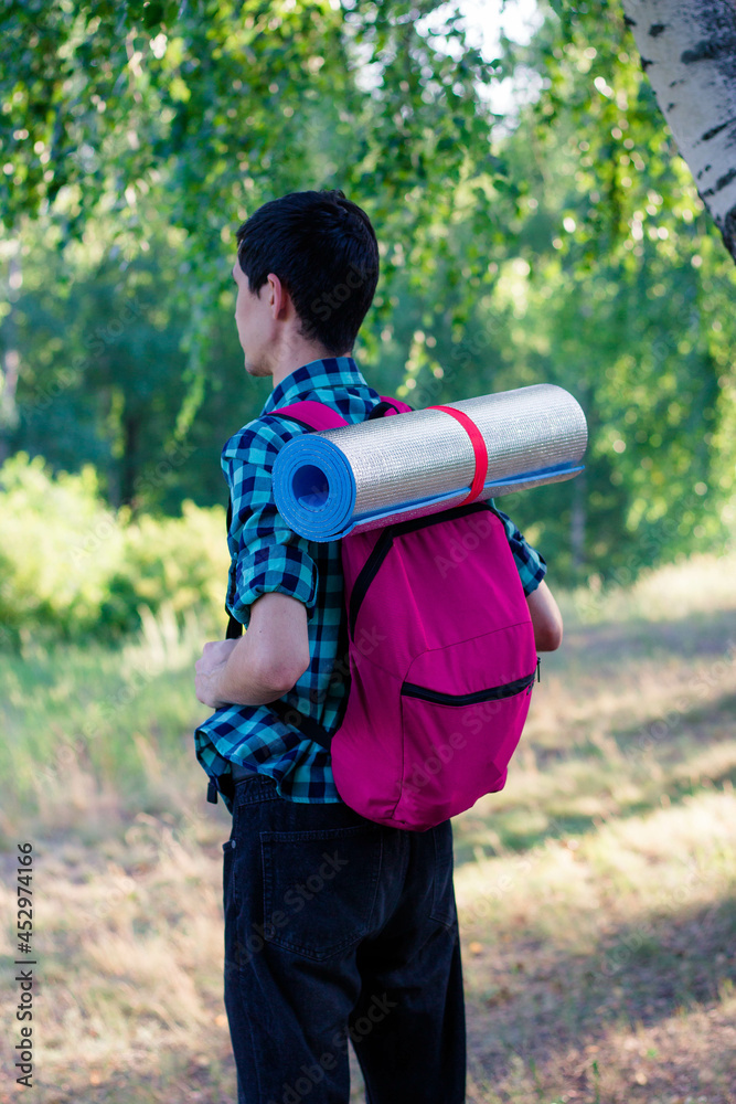 A guy with a backpack and a hiking mat in the woods. Hike in the woods. Travels. Pink backpack.