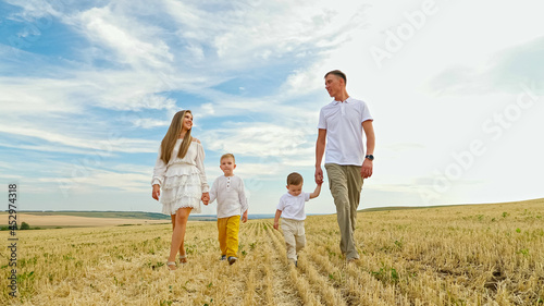 Family father mother and small children sons walk joining hands among field on mown wheat on sunny day under blue sky