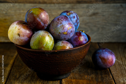 Home harvest fresh plums in a ceramic bowl on a wooden table.