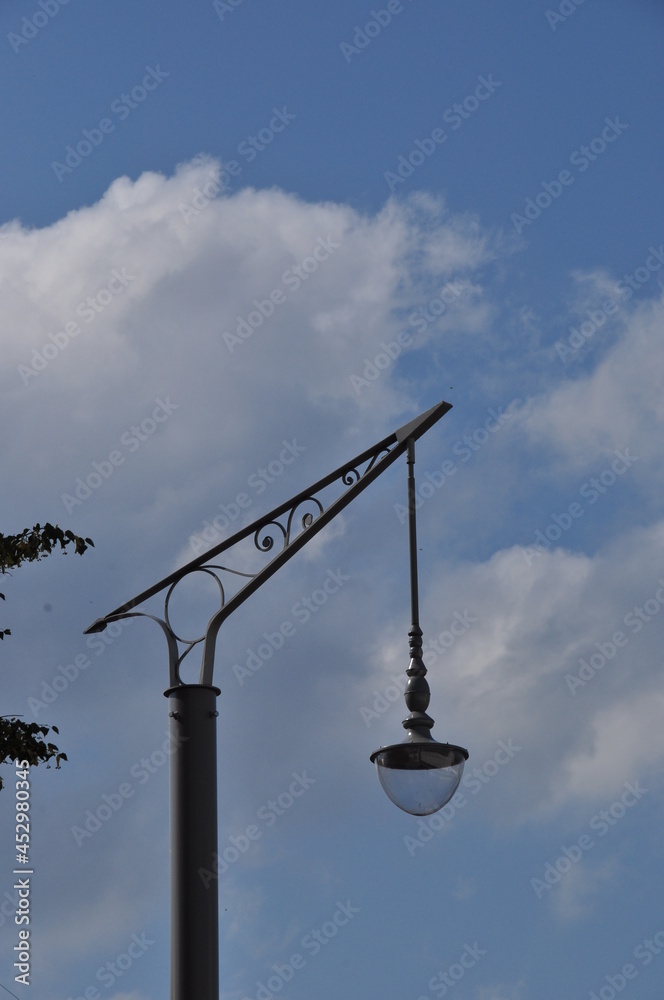 A lamppost with a beautiful lighting lamp. A lamppost against a background of clouds. Summer day. Background, texture, design. A lamppost with a beautiful lighting lamp. A lamppost against a background of clouds. Summer day. Background, texture, design.