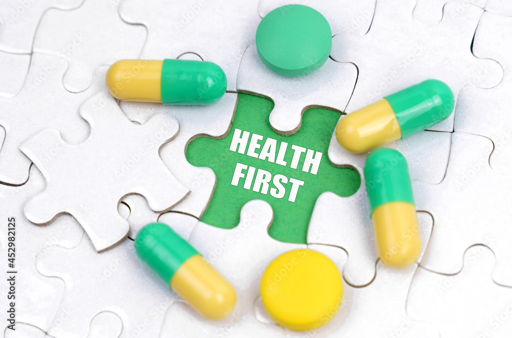 There are pills and vitamins on the white puzzles. Inside on a green background the inscription - HEALTH FIRST There are pills and vitamins on the white puzzles. Inside on a green background the inscription - HEALTH FIRST