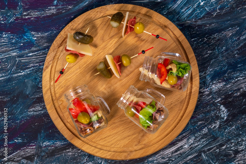 Jarcuterie Snacks in transparent jars cheese ham olives lettuce cucumbers nuts. Flat lay photo