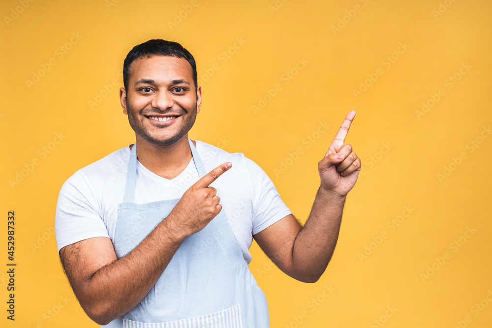 Portrait of happy young good-looking afro american indian cook or chef with smile, pointing aside with finger, with excited face expression isolated over yellow background. Portrait of happy young good-looking afro american indian cook or chef with smile, pointing aside with finger, with excited face expression isolated over yellow background.