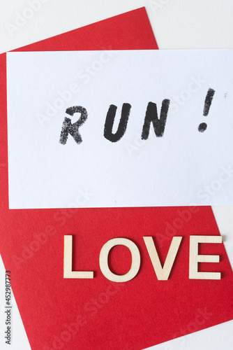 the expression "run!" stencilled in black on white paper, with the word "love" in plain wood letters on a red background