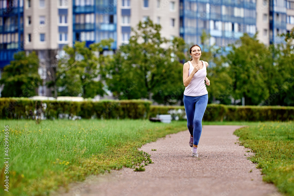 Smiling young woman is running in city garden at daytime.
