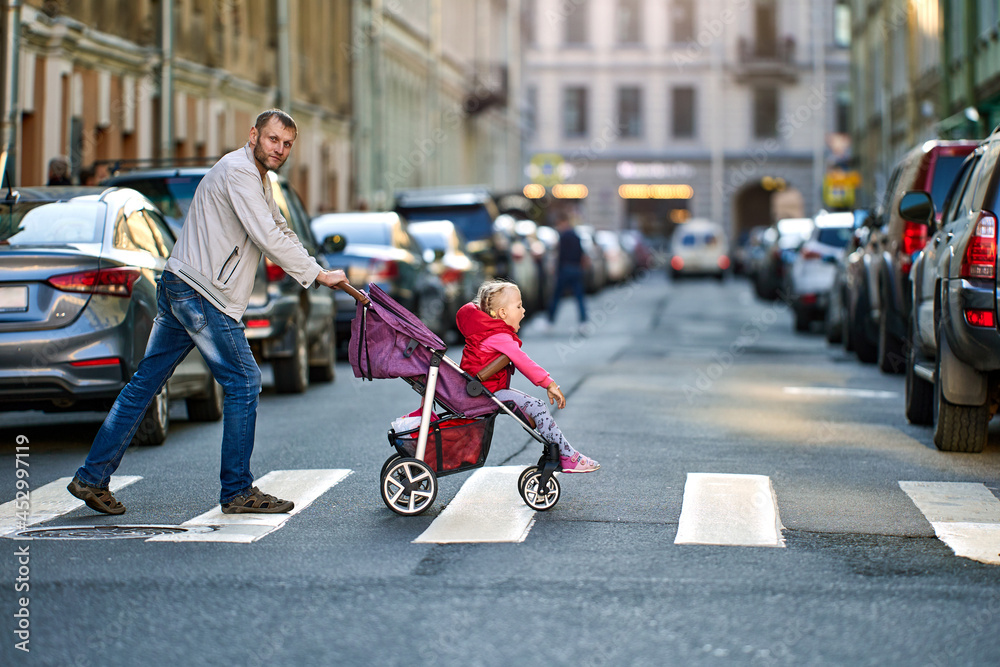 Obraz premium Father drives child in perambulator along pedestrian crossing.