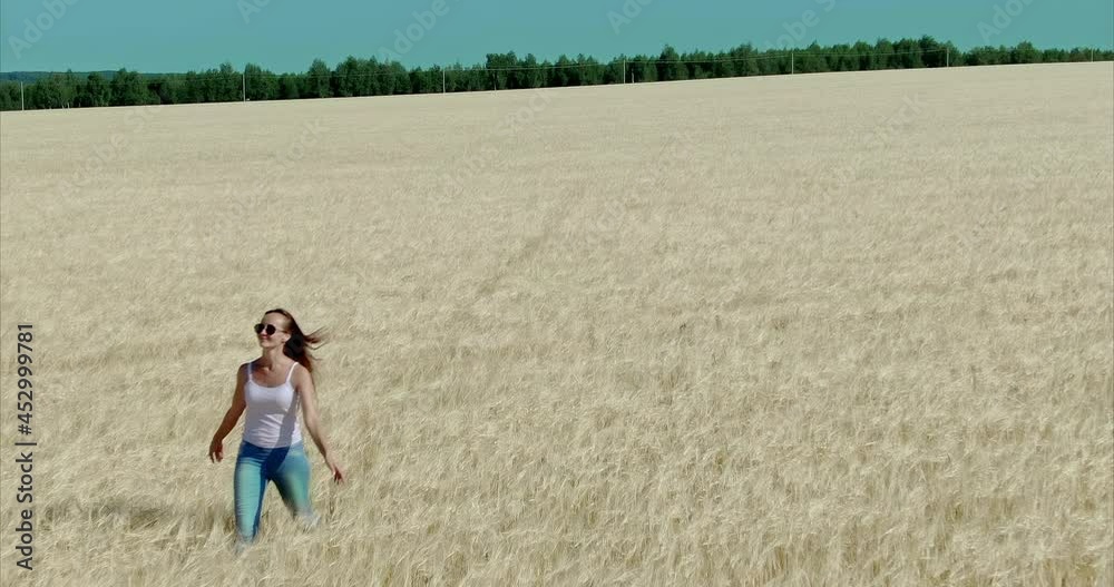 Quadcopter flies over the golden ears of wheat in the field. Beautiful young woman is walking in the field, she is happy. Beautiful landscape, rural. 4k, ProRes Quadcopter flies over the golden ears of wheat in the field. Beautiful young woman is walking in the field, she is happy. Beautiful landscape, rural. 4k, ProRes
