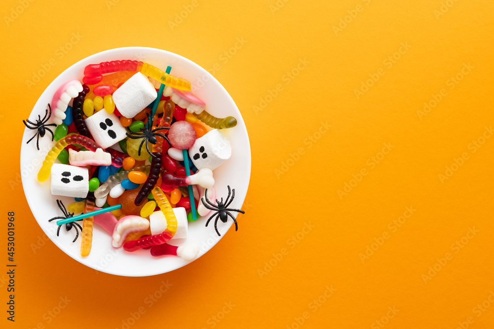 Halloween sweets and decorations in plate on orange background. Happy Halloween holiday concept. Flat lay, top view, copy space.