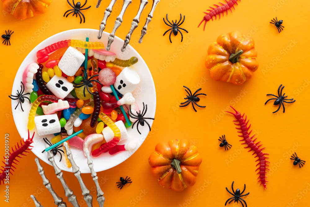 Halloween sweets in plate and decorations on orange background. Happy halloween holiday concept. Flat lay, top view, overhead.