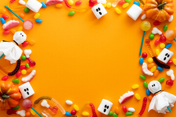 Creative flat lay composition with Halloween sweets and decoration on orange background. Happy halloween greeting card mockup, banner design. Top view with copy space.