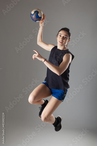 Handball player posing on light gray background. Girl jumping with ball.