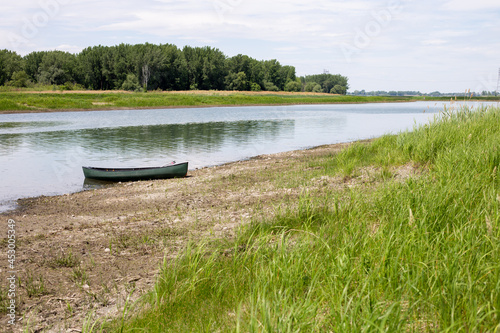 vue d'un canoe vert sur le bord d'une rivière calme en été avec du gazon et des nuages dans le ciel