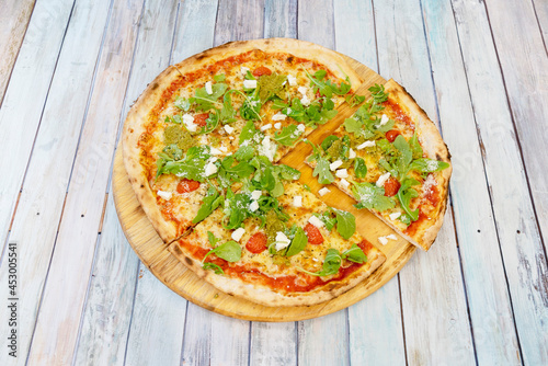 Family pizza cut into pieces with arugula sprouts, fresh cheese, pesto sauce and ripe cherry tomatoes