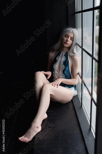 A beautiful young girl in blue pajamas with long hair looks out the window. Fashion and beauty