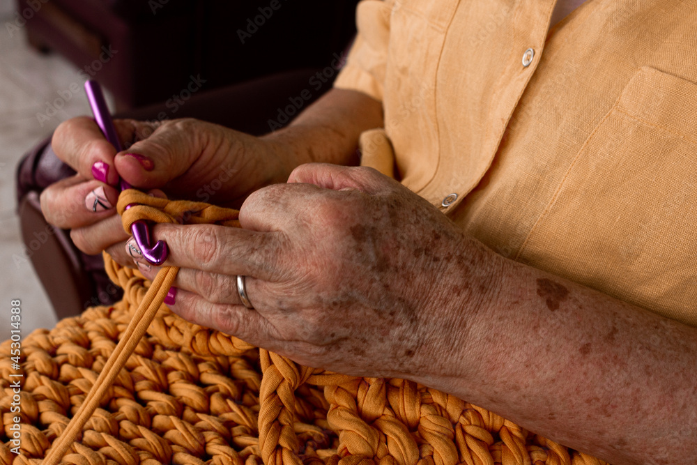  close-up of elderly woman's hands knitting with yellow wool. 