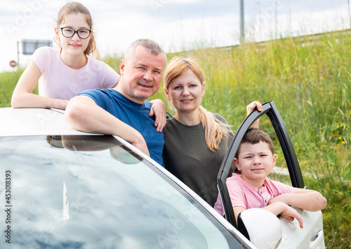 Portrait of happy parents with two teenage children posing together outdoors near car. Family travel concept. © JackF