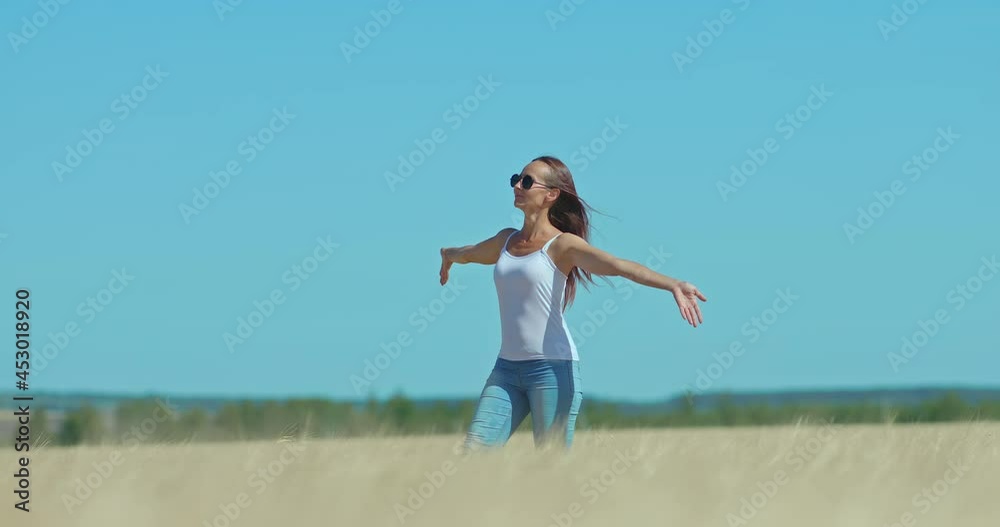 Beautiful girl in sunglasses walks through a wheat field, happy moments of life. Girl walks along the golden field and spreads her hands to the sides, a beautiful landscape. Beautiful girl in sunglasses walks through a wheat field, happy moments of life. Girl walks along the golden field and spreads her hands to the sides, a beautiful landscape.