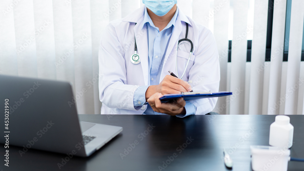 Medical concept a male doctor wearing a mask writing prescription to patient for recovering from Coronavirus (COVID-19) at his modern clinic