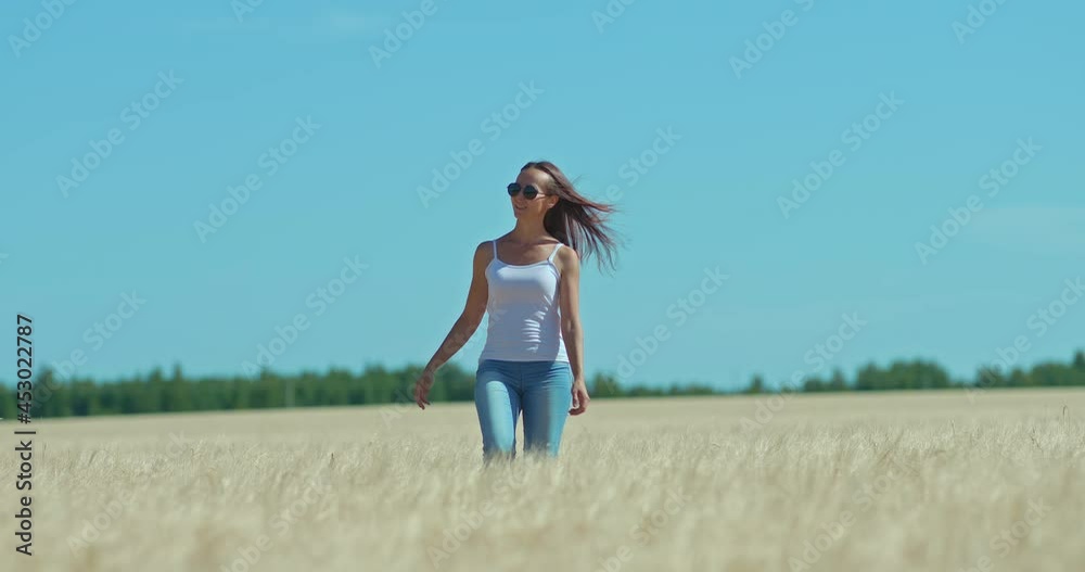 Happy young woman walks in a golden wheat field. Young woman walks across the field and smiles. Blue sky, beautiful landscape. 4k, ProRes Happy young woman walks in a golden wheat field. Young woman walks across the field and smiles. Blue sky, beautiful landscape. 4k, ProRes