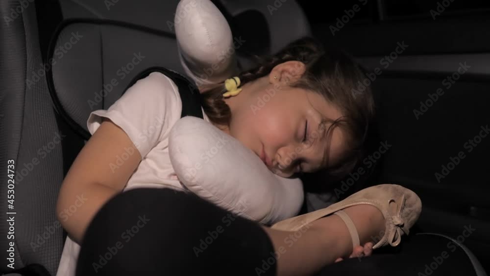 A little girl sleeps in the back seat in a car seat at night. The car is on the road. The child is tired after a long journey by car. Uncomfortable sleeping position. Auto-pillow for sleeping A little girl sleeps in the back seat in a car seat at night. The car is on the road. The child is tired after a long journey by car. Uncomfortable sleeping position. Auto-pillow for sleeping