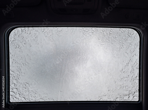 Inside a vehicle looking up to a sunroof with water droplets  photo