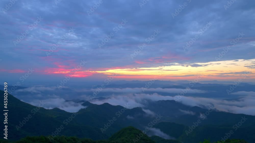 In the early morning, flowing clouds and fog among mountains, slow sunrise, and dark clouds moving in sky, time-lapse