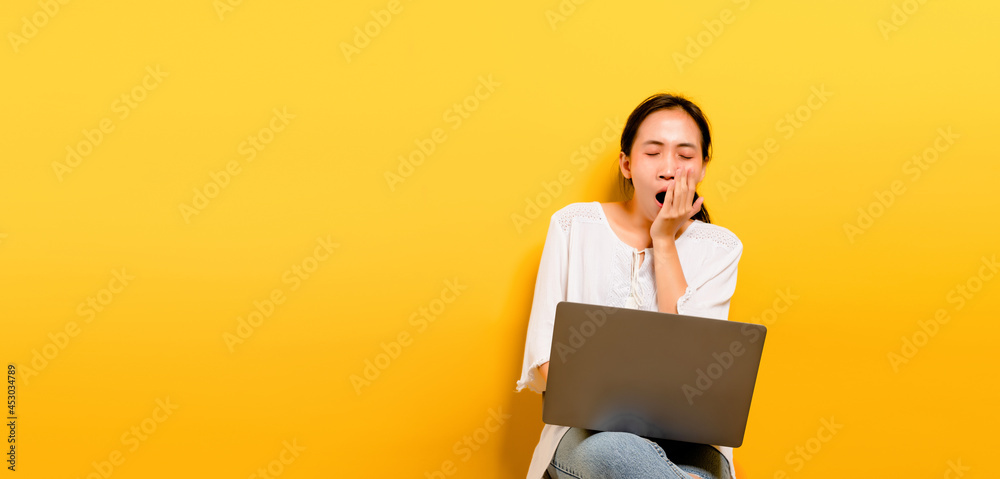 Asian woman working on laptop computer and showing drowsiness from work hard work concept on a yellow background in the studio Asian woman working on laptop computer and showing drowsiness from work hard work concept on a yellow background in the studio