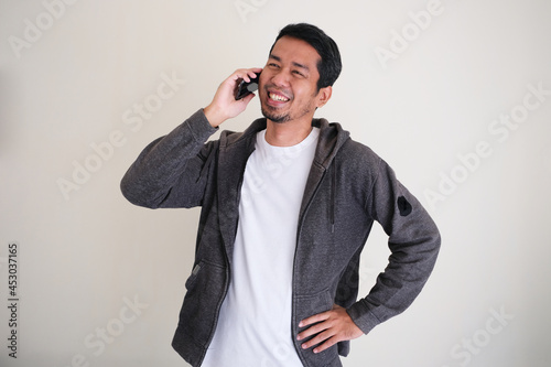 Attractive Asian man smiling happy while calling someone with his hand on waist photo