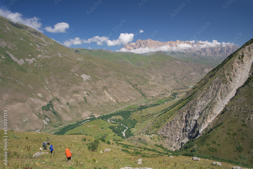 Hikers with backpacks go down the slope of a mountain valley.
