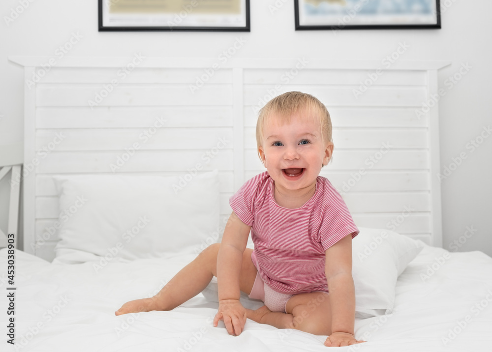 Happy caucasian baby girl about 1 year old having her two first milk teeth laughing sitting on bed.Adorable child playing indoors,kid having fun before going to bed, after waking up or toothing idea Happy caucasian baby girl about 1 year old having her two first milk teeth laughing sitting on bed.Adorable child playing indoors,kid having fun before going to bed, after waking up or toothing idea