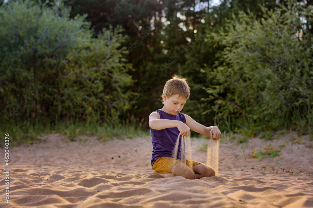 cute caucasian boy of elementary age sifting sand on beach on summer sunset cute caucasian boy of elementary age sifting sand on beach on summer sunset