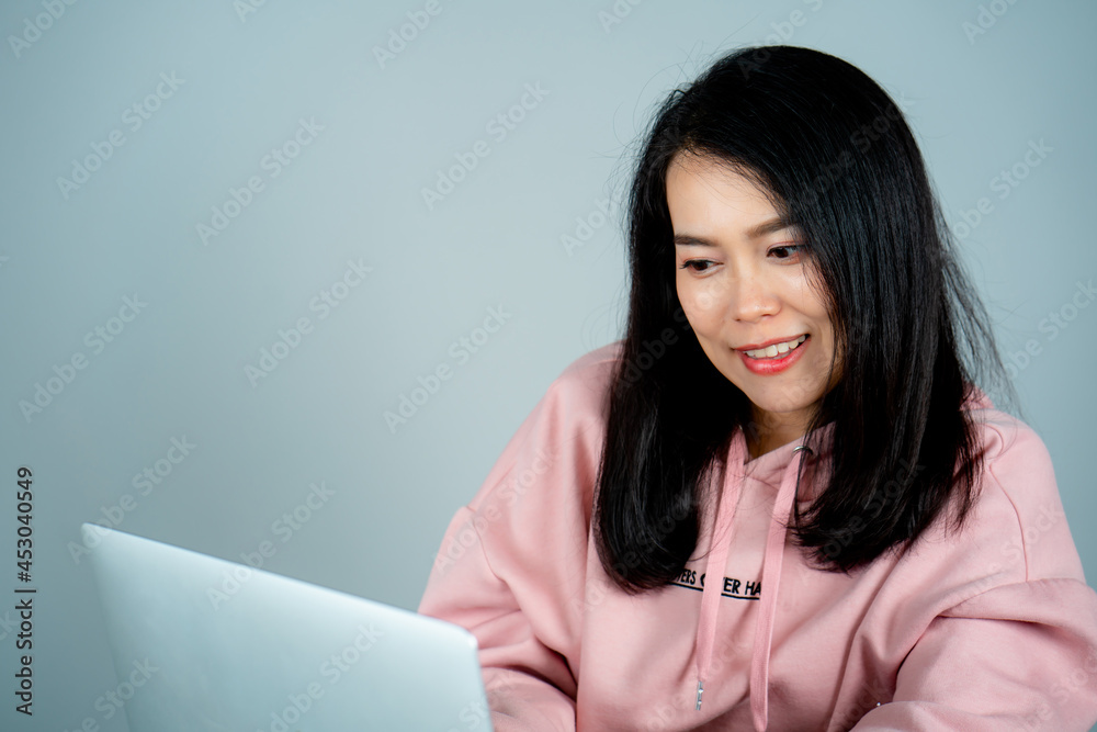 Portrait of an Asian girl wearing a pink shirt. sitting on a laptop computer online shopping with a happy face behind a gray studio background Portrait of an Asian girl wearing a pink shirt. sitting on a laptop computer online shopping with a happy face behind a gray studio background