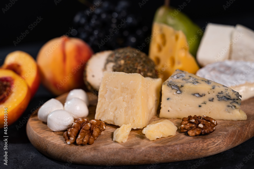 Close Up Still Life of Variety of Gourmet Cheeses with Soft Melting Cheese Round in Foreground with Fruit Garnish on Dark Rough Textured Background with Copy Space