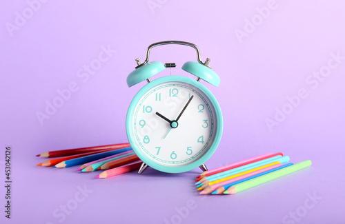 Stylish alarm clock and pencils on color background