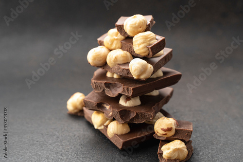 Delicious milk chocolate bars with nuts on black table close up. Stack of chocolate slices Hazelnut and almond milk chocolate pieces tower. Sweet food photo concept. Chunks of broken chocolate