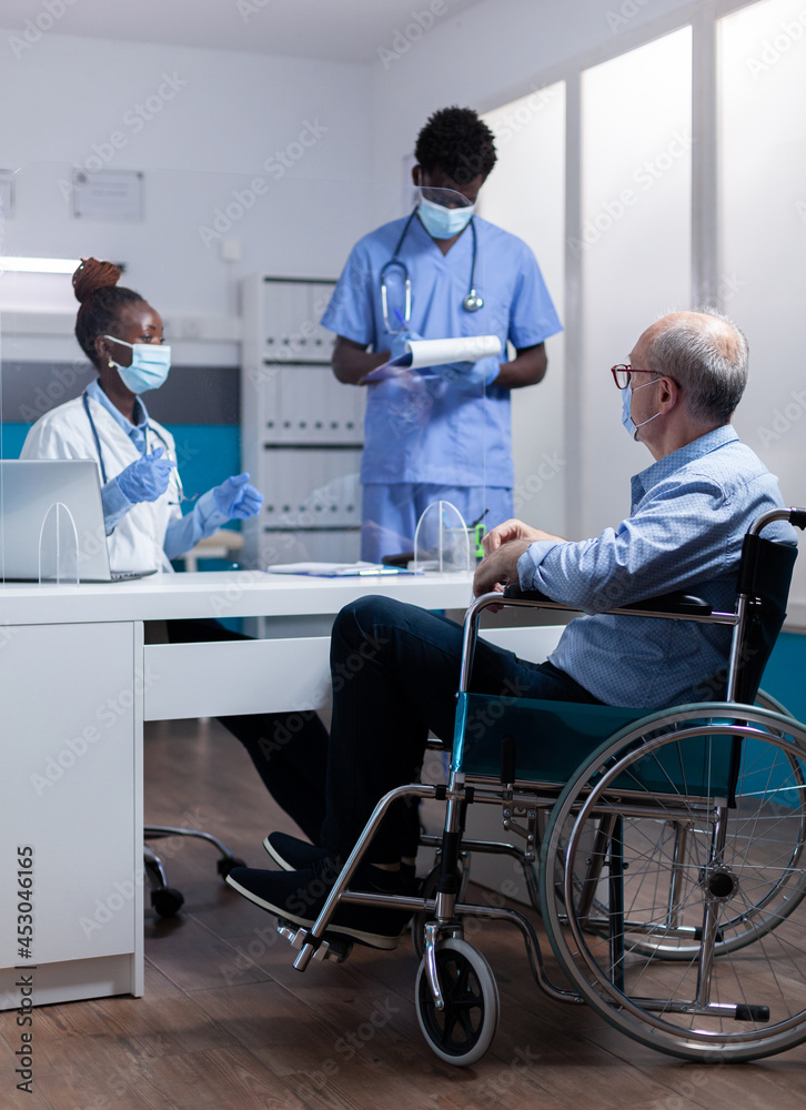 Professional african american team discussing healthcare diagnosis with disabled old patient. Black doctor and nurse talking to sick elder man with handicap sitting in wheelchair Professional african american team discussing healthcare diagnosis with disabled old patient. Black doctor and nurse talking to sick elder man with handicap sitting in wheelchair