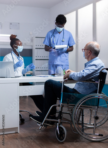 Professional african american team discussing healthcare diagnosis with disabled old patient. Black doctor and nurse talking to sick elder man with handicap sitting in wheelchair