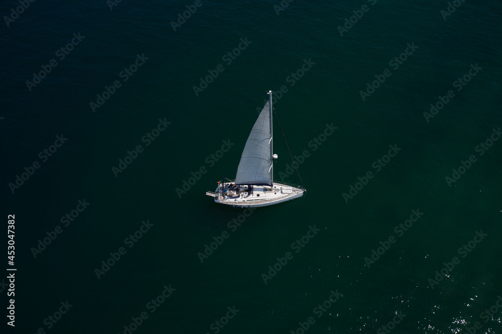 Large white boat with sails on blue water aerial view. Lonely sailboat on the water top view. Boat with sails, blue water with high altitude. Sailboat on Lake Garda, Italy.