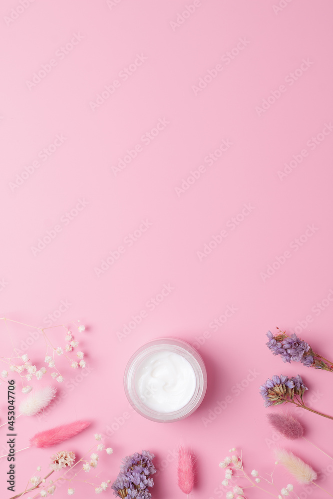 Jar of cosmetic cream with flowers on pink background. Flat lay, copy space