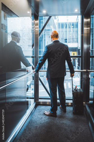 Businessman on a business trip arrived at the hotel for settlement rises in elevator standing with his back to the camera holding a suitcase by the handle. Business man looking outside of the window. 