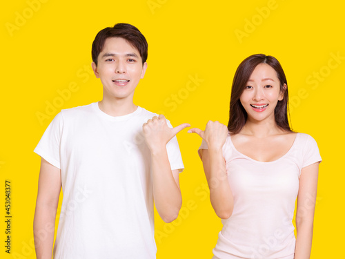 Young couple point at each other with thumbs.Isolated on yellow background.