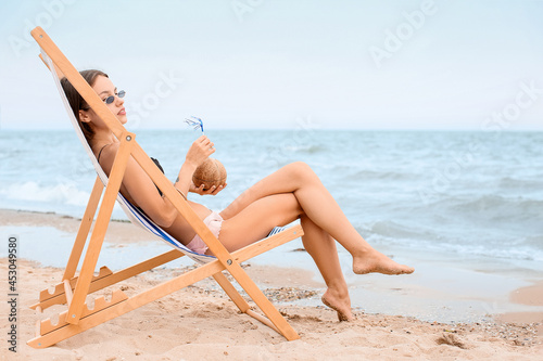 Beautiful young woman drinking coconut milk on sea beach