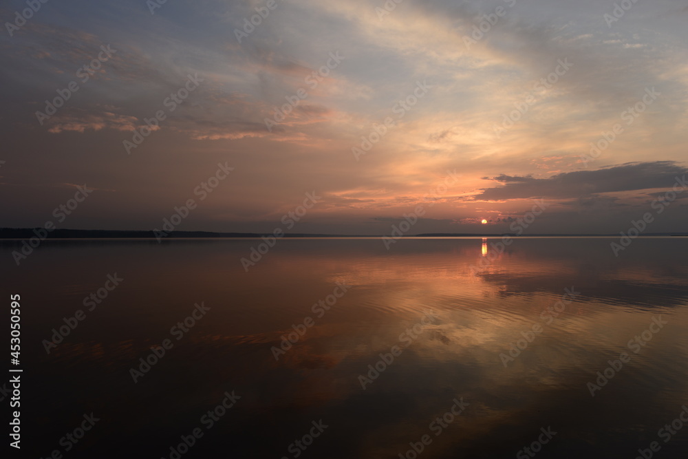 Sunset in the clouds on the horizon over the calm water of the lake