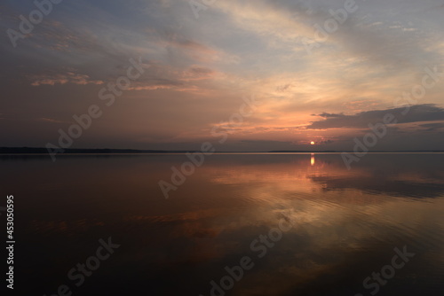Sunset in the clouds on the horizon over the calm water of the lake