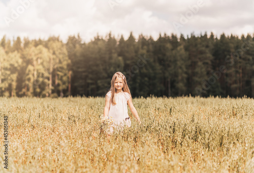 A little blonde girl walks through a golden field in the summer. Concept of purity, growth, happiness